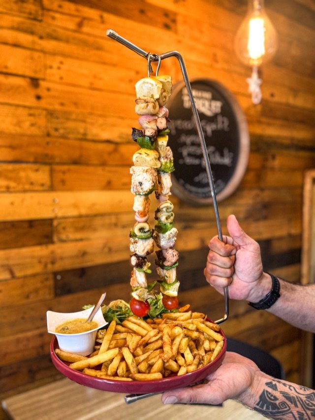 Brochette de gambas et frites présentée à la main, salle du Belem
