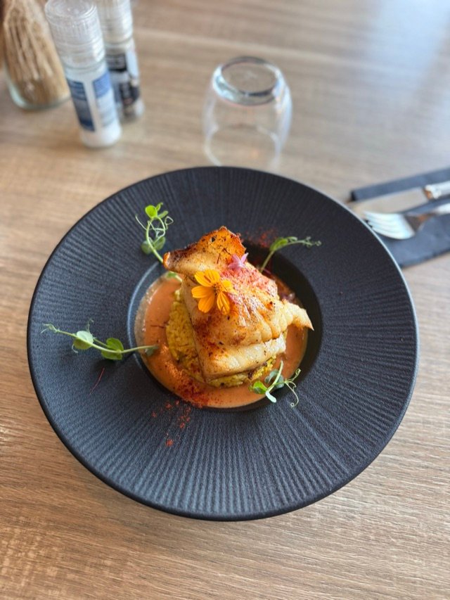 Plat de poisson dressé dans une assiette noire, vue de dessus