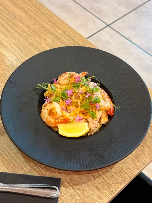 Assiette de pâtes aux crevettes et poisson, fleurs comestibles et quartier de citron