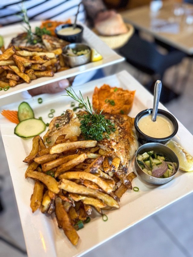 Deux assiettes de poisson grillé, frites maison, purée de patate douce et sauce