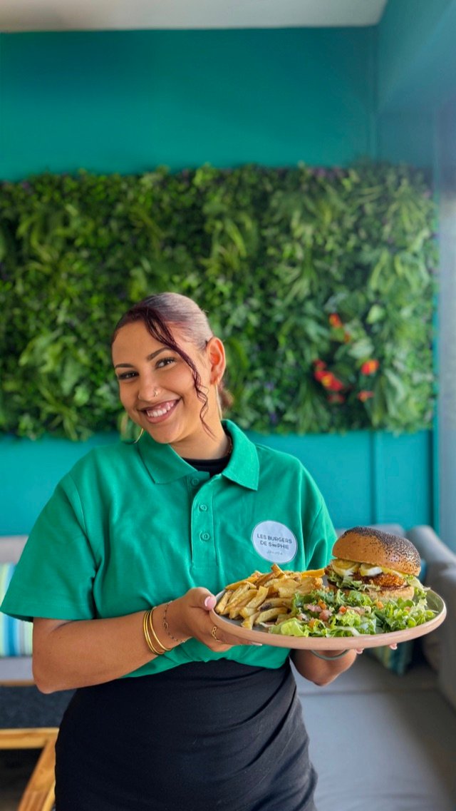 Membre de l'équipe présentant une assiette burger-frites devant le mur végétal
