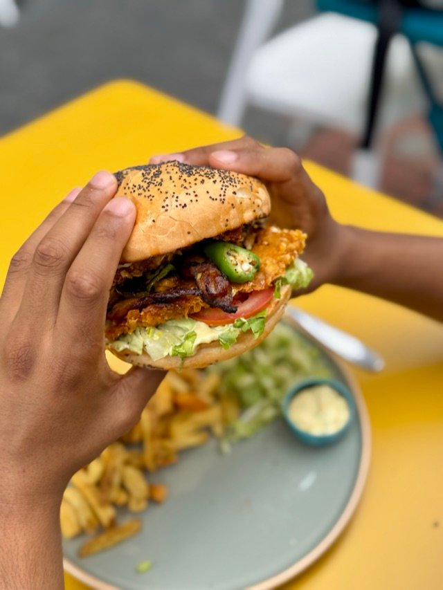 Burger tenu à deux mains au-dessus de son assiette, table jaune