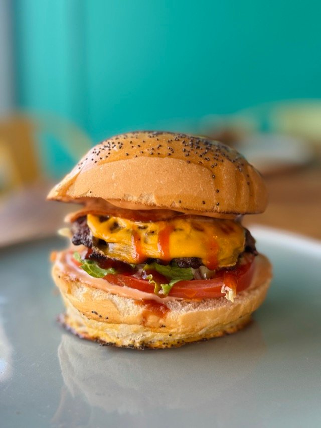 Burger au cheddar fondu, tomate et salade, vu de profil