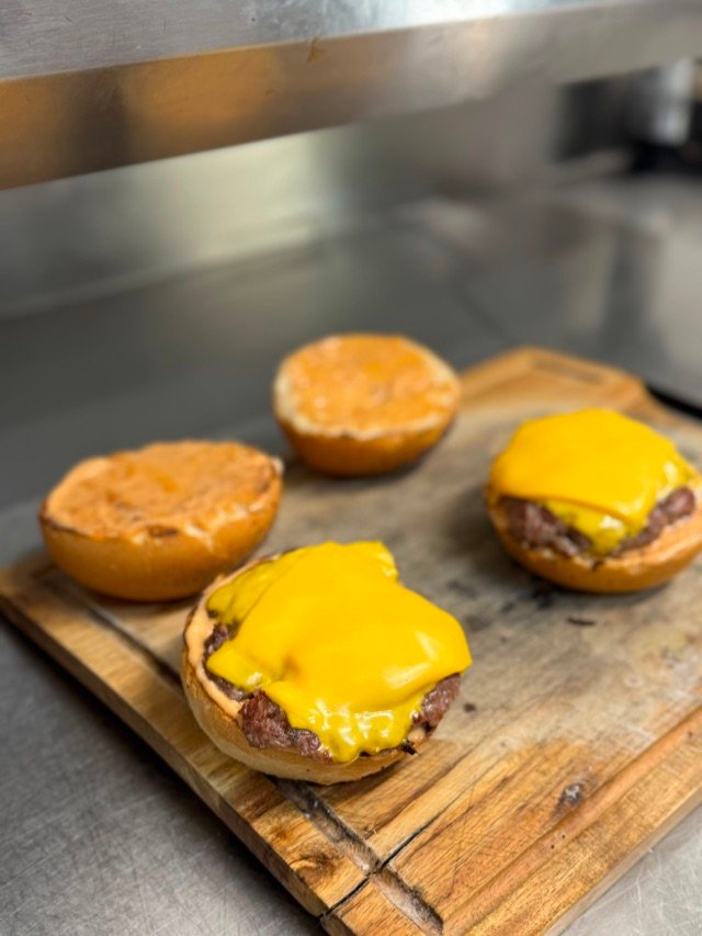 Trois pains toastés et deux steaks au cheddar fondu, sur la planche de la cuisine