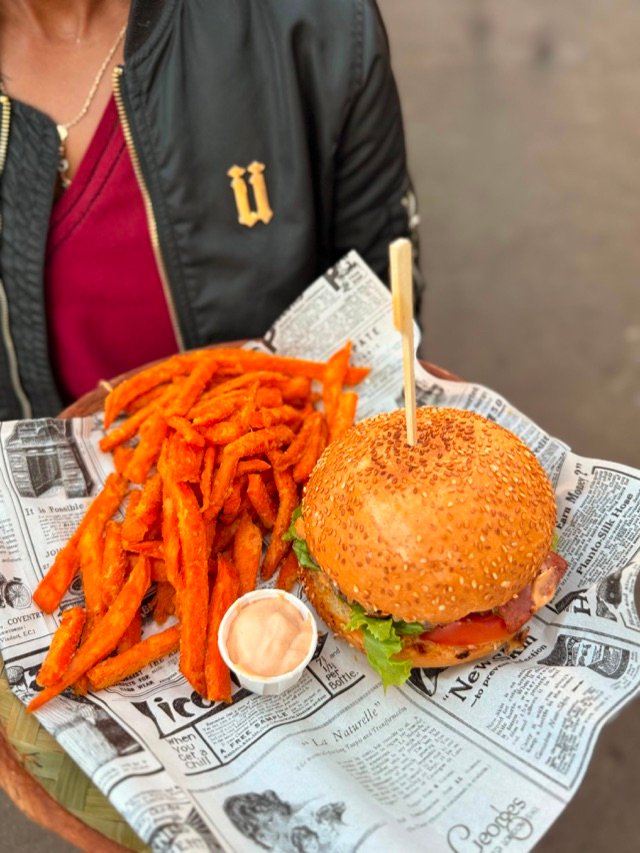 Burger au sésame et frites de patate douce servis sur papier journal, à emporter