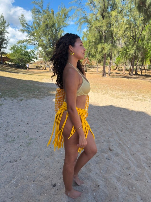 Jupe en macramé jaune à franges portée sur un maillot vert clair, sur le sable