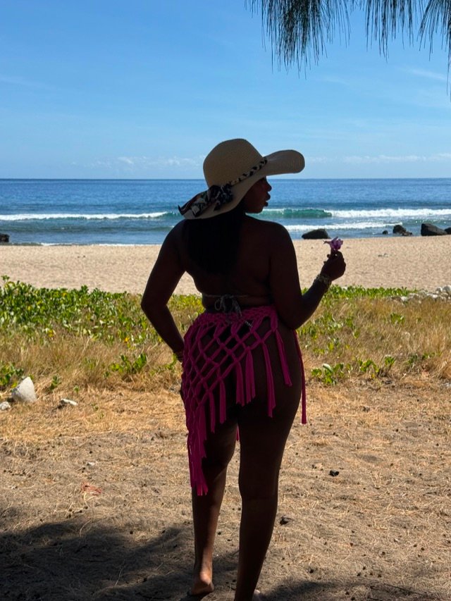 Jupe en macramé fuchsia et capeline, à contre-jour devant le lagon