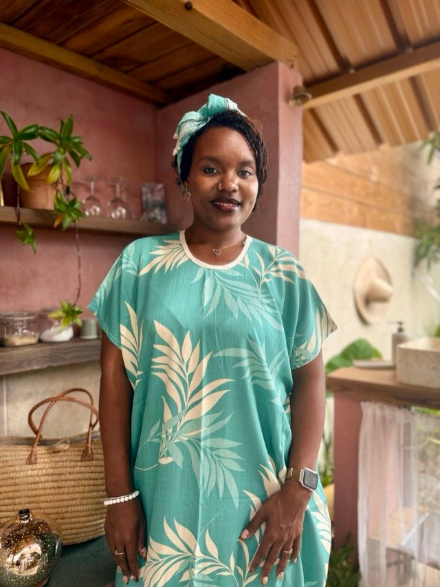 Robe longue vert d'eau à motif de feuillages, portée avec un foulard assorti, sous une varangue