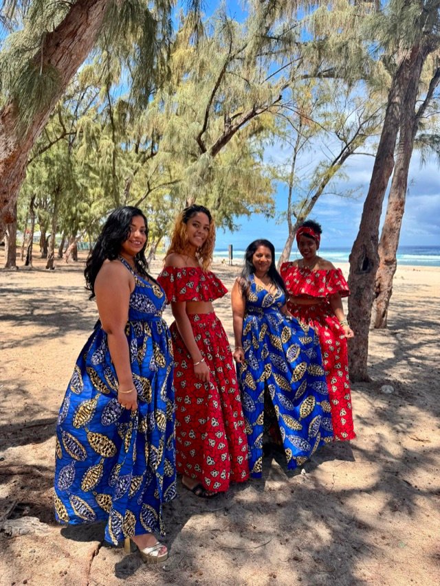 Quatre tenues en wax bleu et rouge portées ensemble sous les filaos