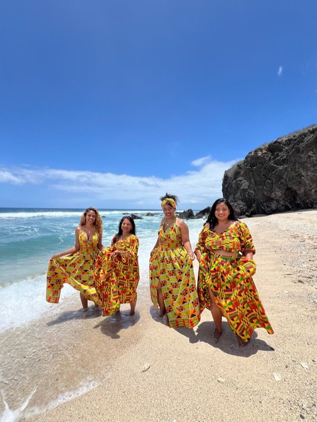 Quatre tenues en wax jaune et vert, les pieds dans l'eau