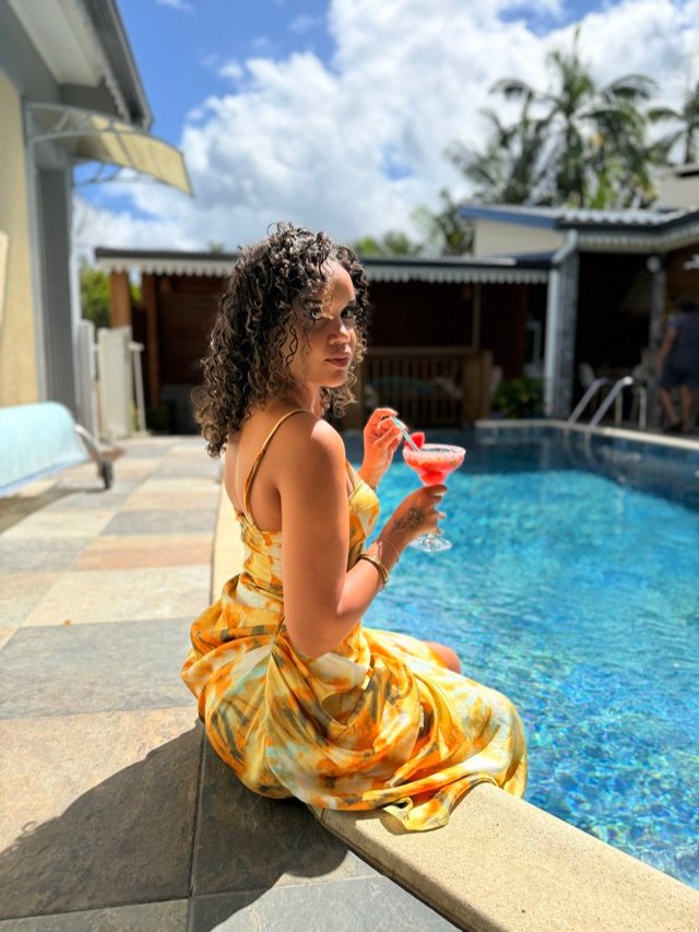 Vue sur la piscine et les cases depuis la terrasse, cocktail à la main