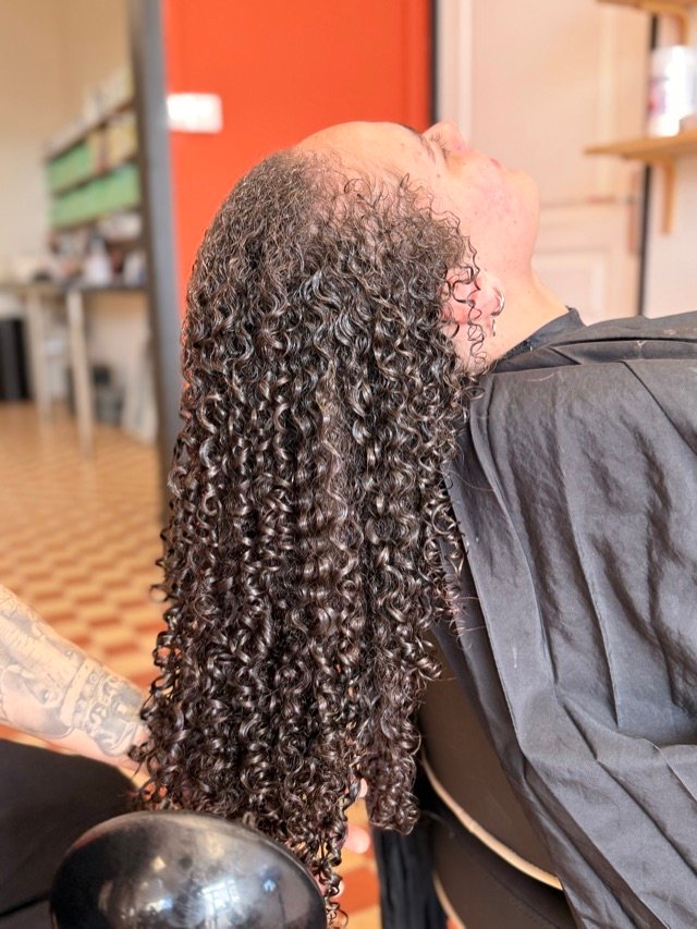 Longue chevelure bouclée définie, vue de dos, au bac du salon